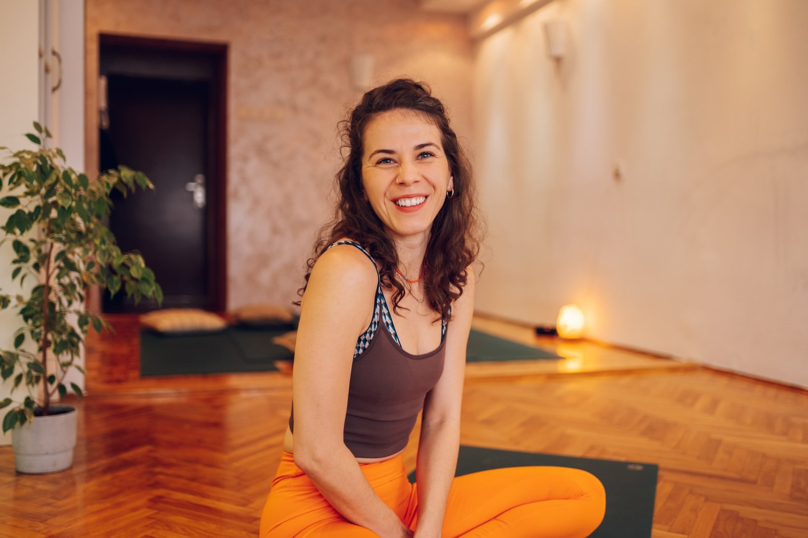 Portrait of a beautiful young woman sitting on the mat in her cozy yoga studio.